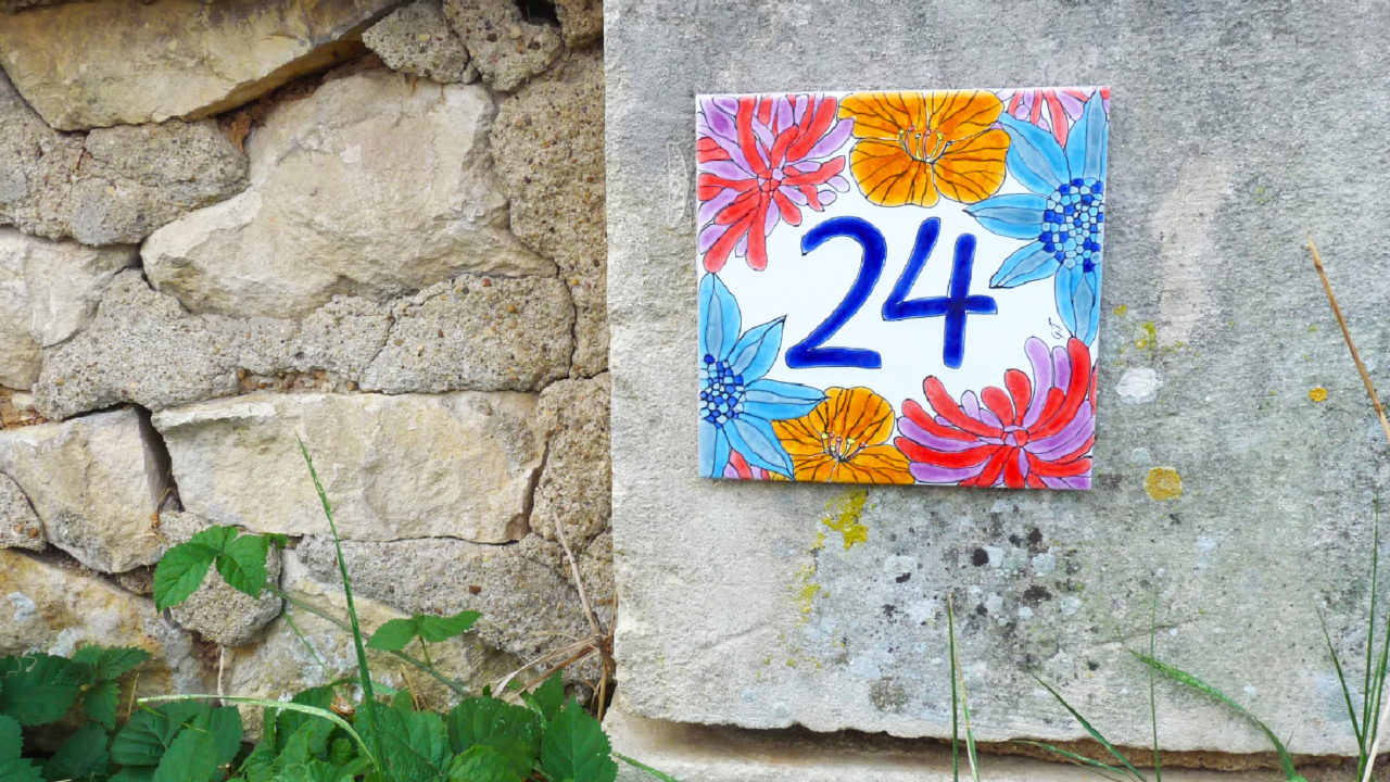 Numéro de maison céramique numéro 24 sur mur en pierre fleurs orange rose rouge bleu