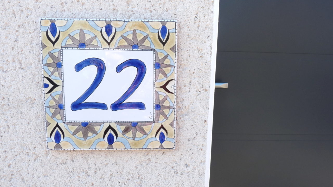 Numéro de maison céramique beige motifs abstraits bleus bruns symétriques numéro d'exemple 22 sur vieux mur de pierre à côté porte portail maison