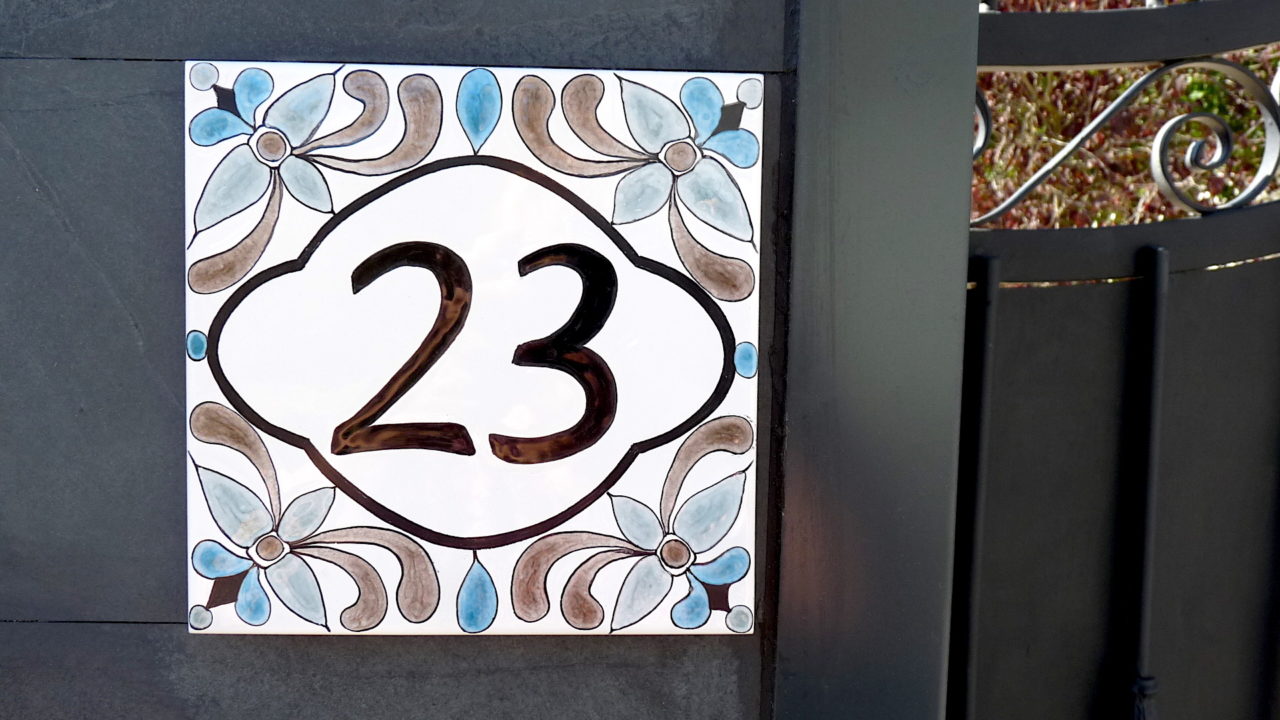 Numéro de maison céramique sur portail noir fond blanc motifs florales symétriques design original personnalisable numéro d'exemple 23