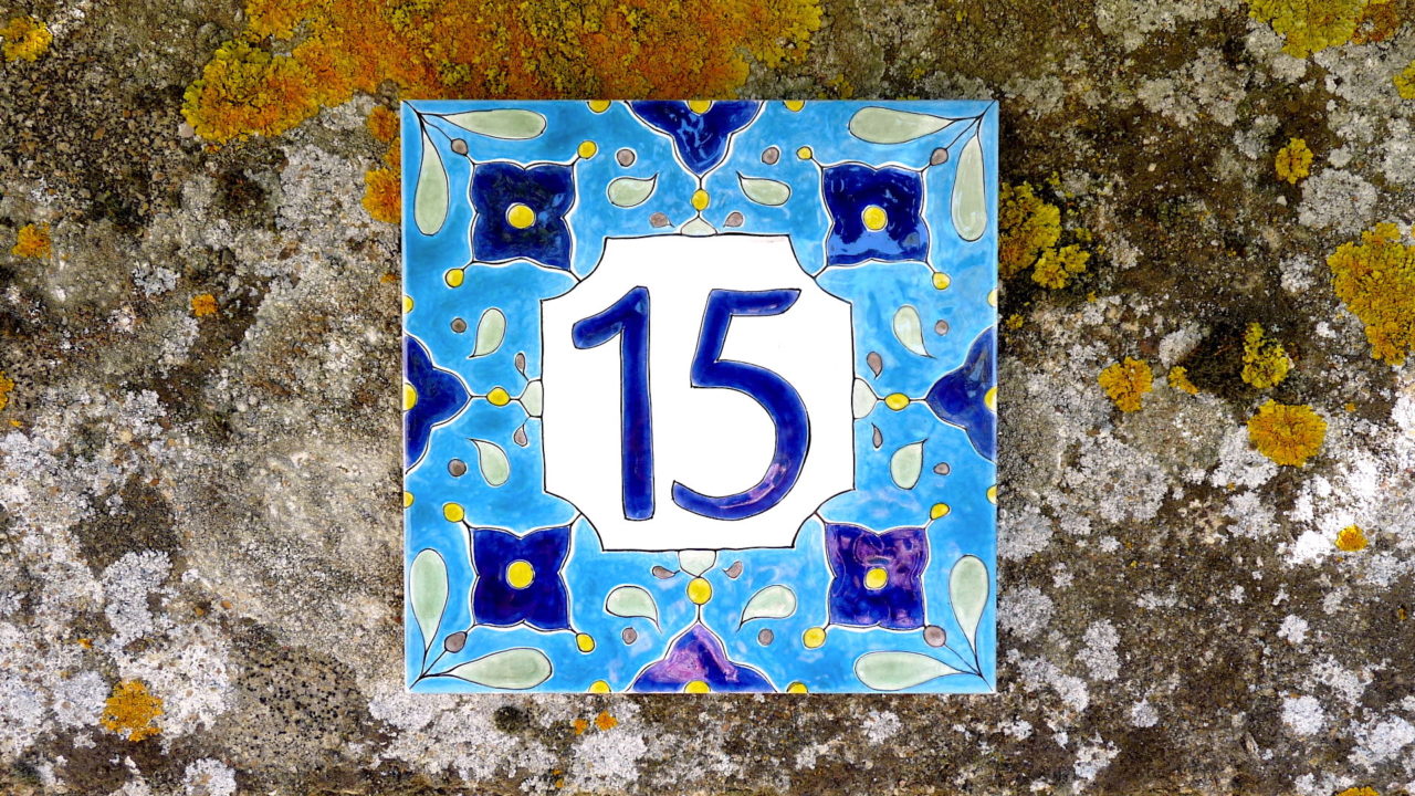 Numéro de maison céramique bleu avec motifs symétriques bleus foncés et jaune design personnalisable original sur mur en pierre mousses