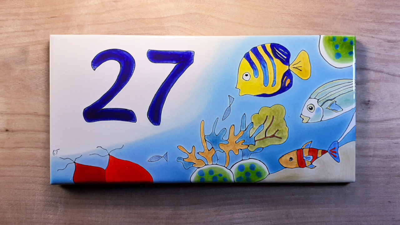 Numéro de maison céramique mer motifs coraux mer poissons sur fond bleu design original numéro d'exemple 27 sur table en bois